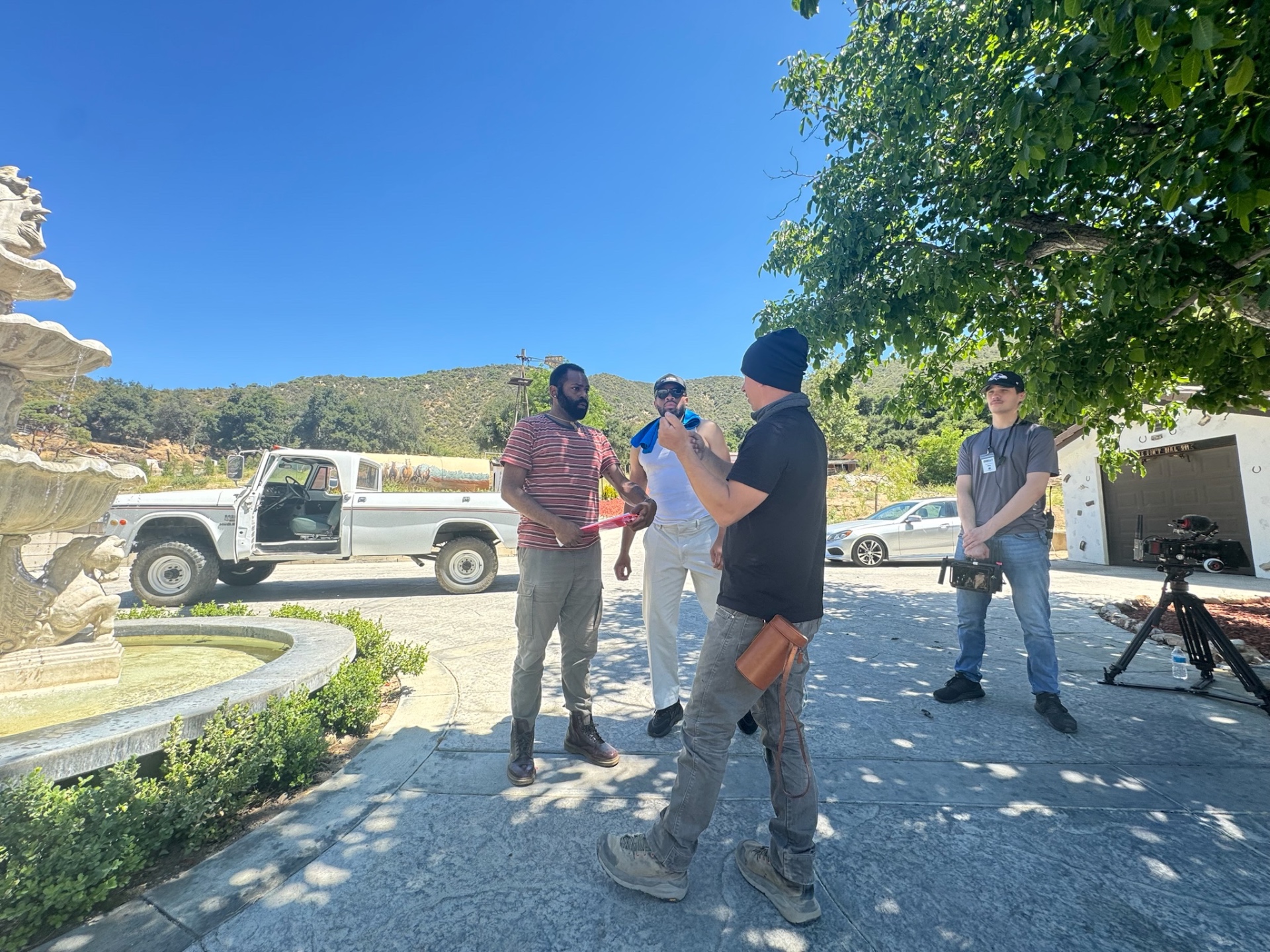 Dogbelly cast and crew gathered by a stone fountain on location for a briefing.