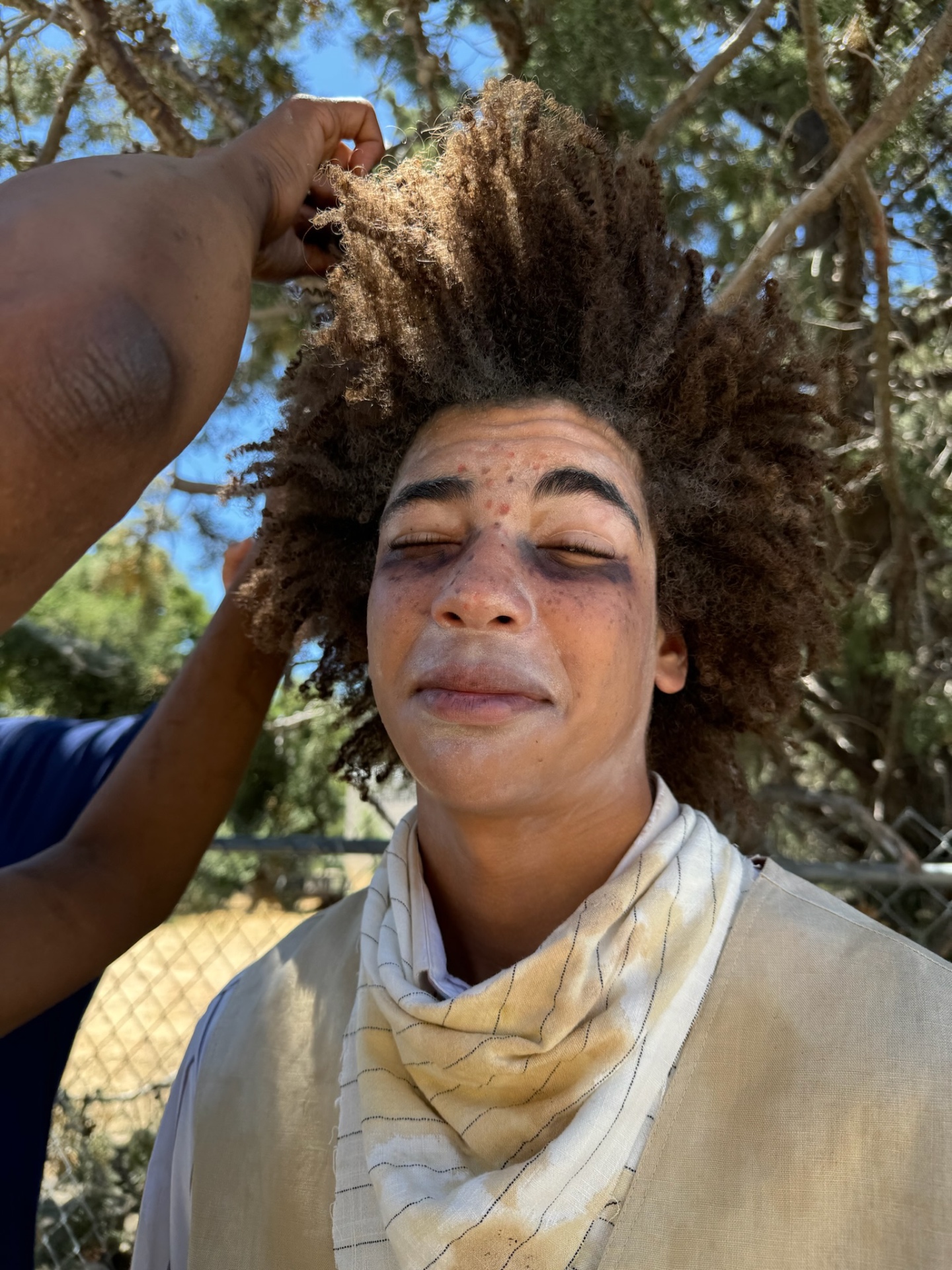 Dogbelly cast member with volumized hair and prosthetic bruises during a makeup touch-up.